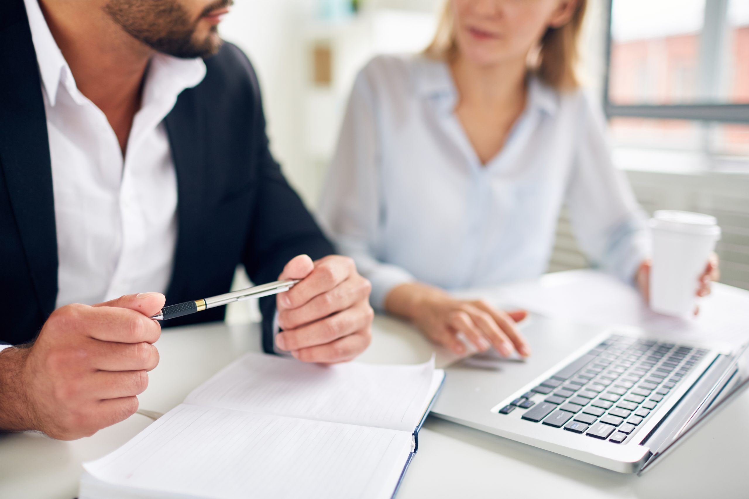 Hands of businessman with pen over open notebook during interaction with colleague